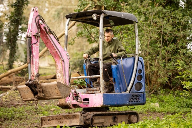 Karl Head of Maintenance on a digger in Finet's Woodland at Solton Manor, Dover, Kent, England planting an apple tree in the old Orchard