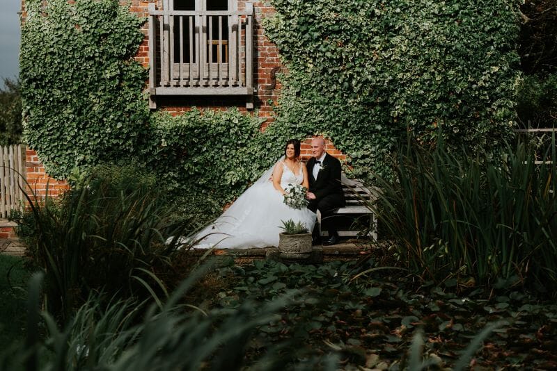 A couple sit bathed in sunlight in front of the Dovecote next to the moat at Solton Manor, Dover, Kent, England