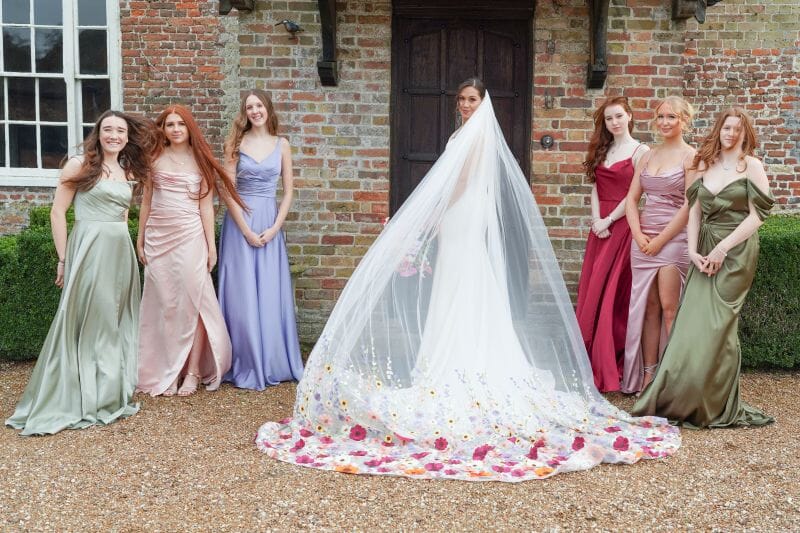 A bride with a sweetpea decorated veil stands with her bridesmaids in front of the porch of Solton Manor Dover