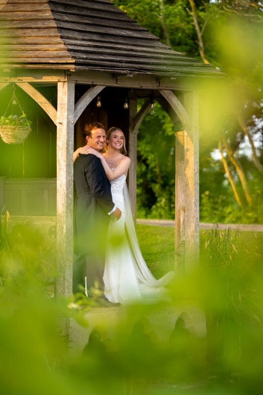 Wedding couple standing in the summer house beside the wildlife pond at Solton Manor, a Kent country manor wedding venue with tranquil gardens and natural outdoor photo locations