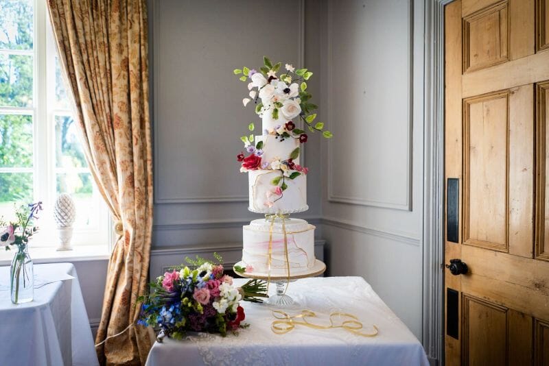 A stunning wedding cake set up with a bouquet next to it inside Solton Manor near Dover
