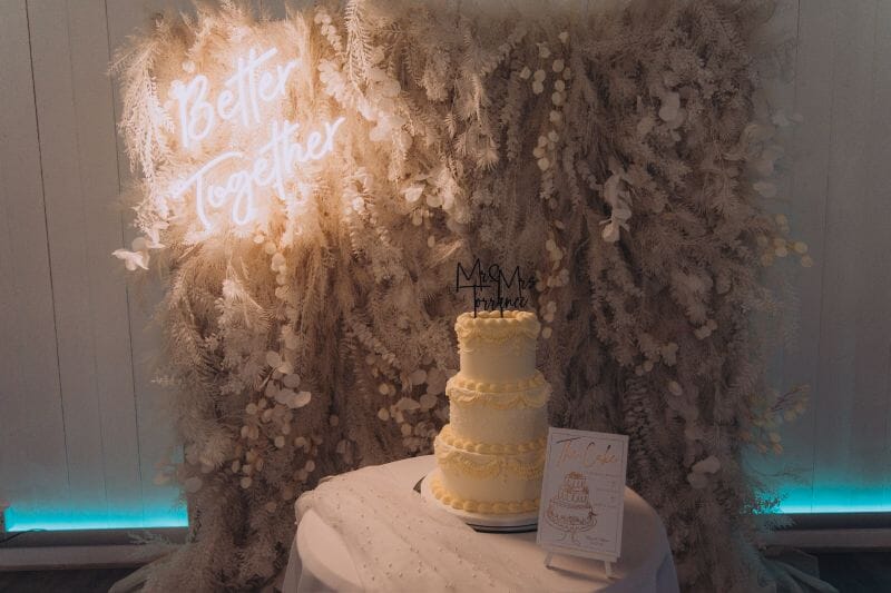 A wedding cake and flower wall set up in the Dutch Barn at Solton Manor, Dover, Kent, England