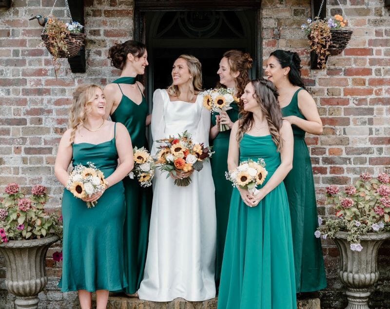 A brides stands with her bridesmaids dressed in teal under the porch of the Solton Manor House in Dover, Kent, England