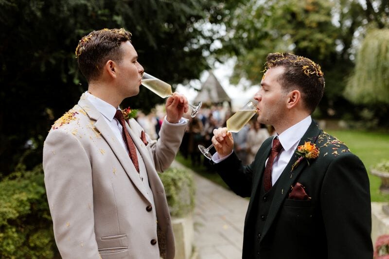 Two grooms enjoy a glass of bubbles after their ceremony in Godric's Garden at Solton Manor, Dover, Kent