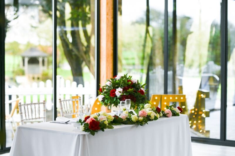 Events In Bloom faux flowers on a sweetheart table in the Dutch Barn at Solton Manor