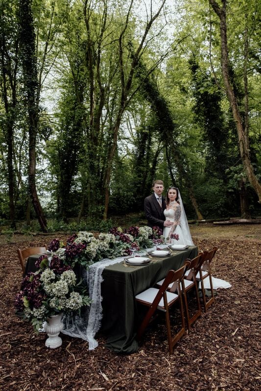 A just married couple stand next to a tablescape set up in the woodlands at Solton Manor, near Canterbury, Kent, England