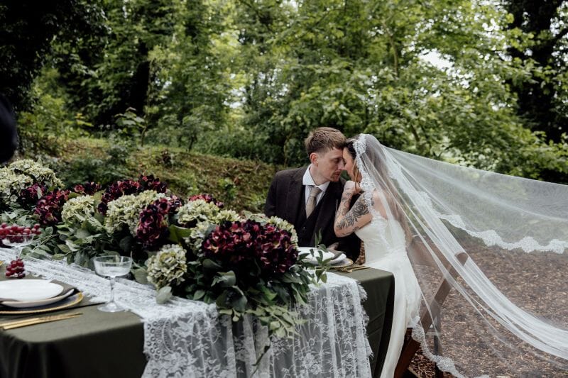 A couple sit next to a tablescape set up in the woodlands at Solton Manor, near Canterbury, Kent, England