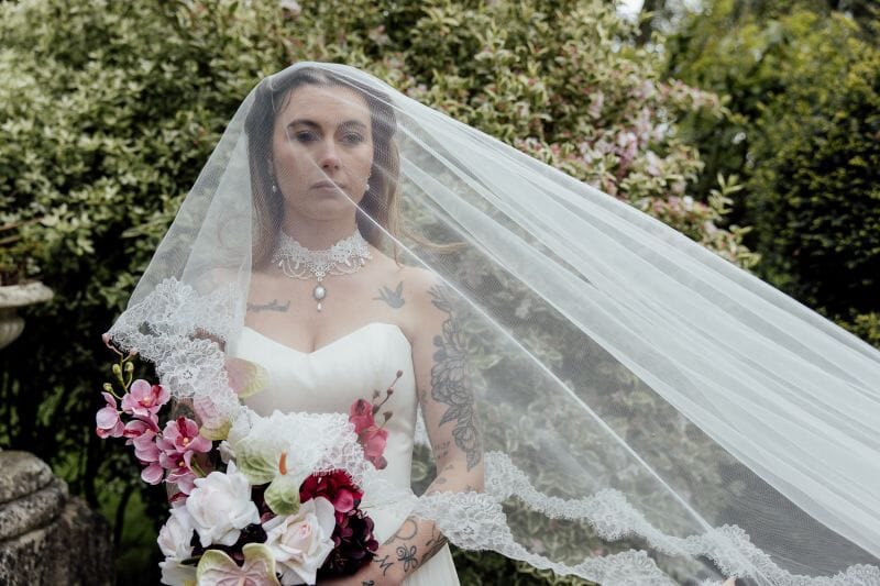 A veiled tattooed bride stands with her bouquet in the grounds of Solton Manor, near the White Cliffs of Dover, Kent, England