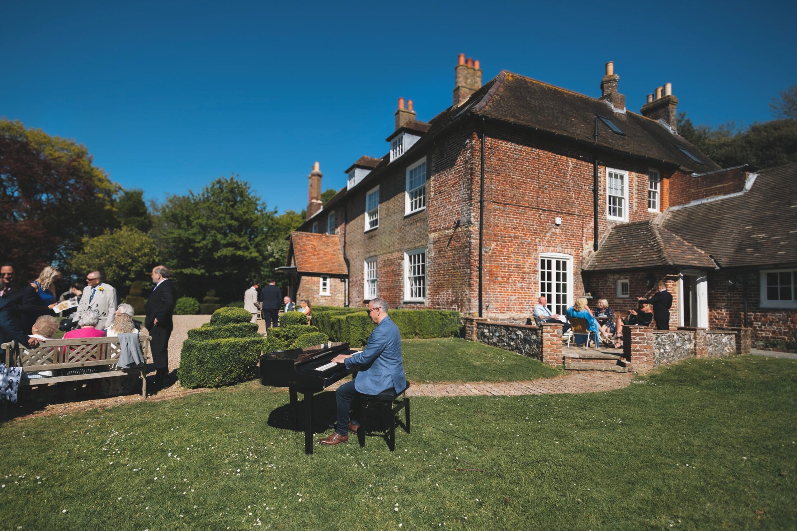 Bryan Emery playing piano on the front lawn during the wedding drinks reception at Solton Manor, East Langdon, Dover, Kent, England