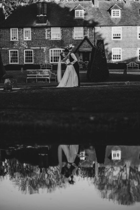 A couple stand in front of the manor house with a wildlife pond reflection in Black and White at Solton Manor