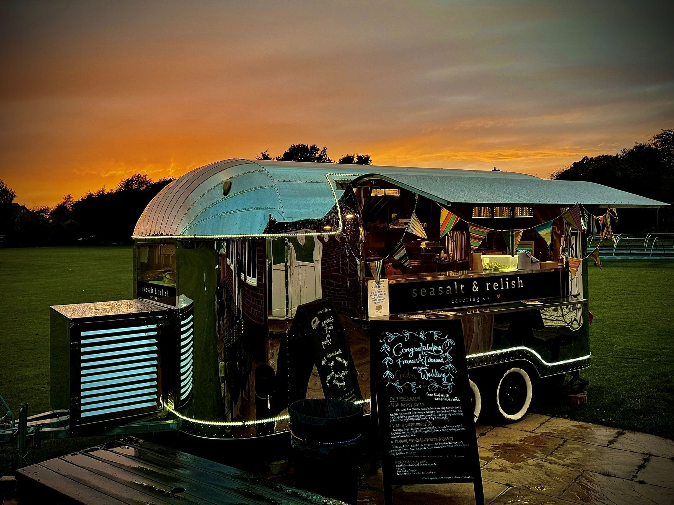 A beautifully restored silver bullet food station set against the backdrop of Famine Field at Solton Manor, St Margaret's Bay. As the sun begins to set, guests can gather for freshly prepared food served from this striking vintage trailer, creating a relaxed and sociable focal point for the evening celebrations.