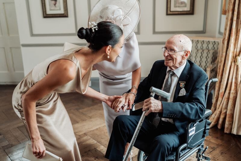 A bridesmaid greats a guest in a wheel chair in the gallery at Solton Manor, Dover, Kent, England